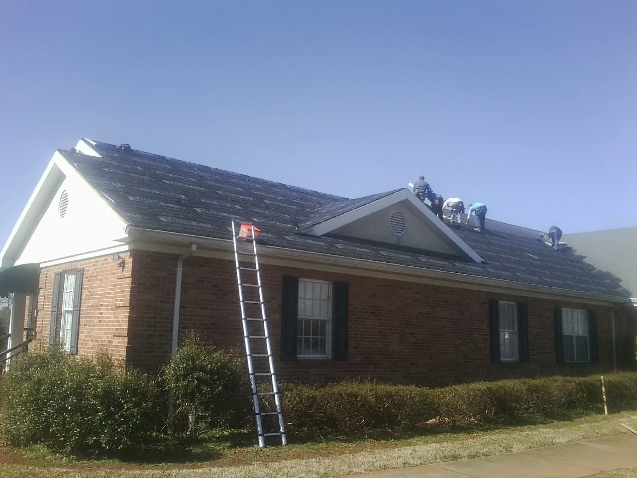 Crew tearing shingles off a brick ranch roof with a ladder set — Emergency Roof Repair work by our crew in East Prospect