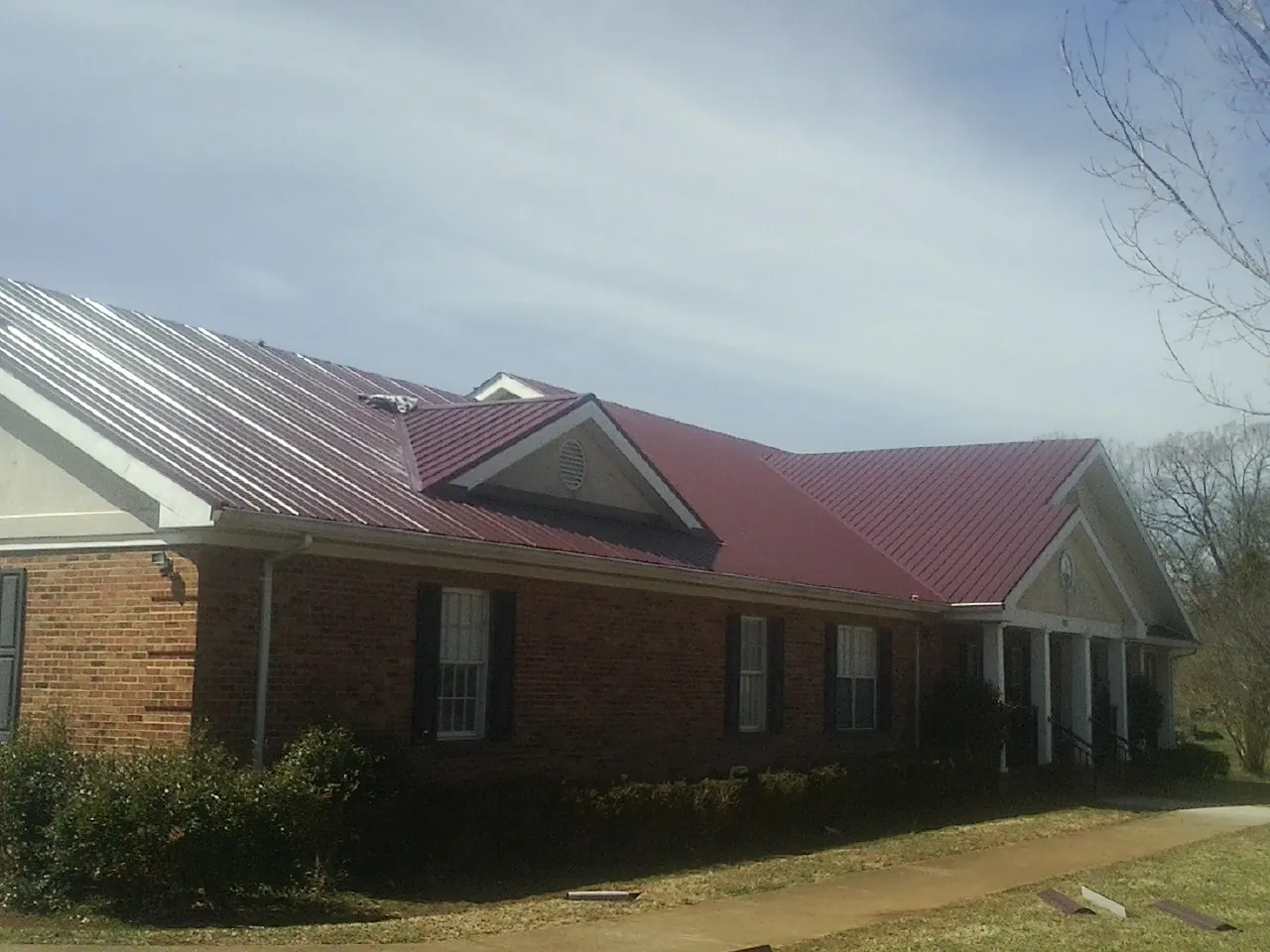Red metal roof with gabled entries on a long brick building, from a Hail Damage Roof Repair job in East Prospect