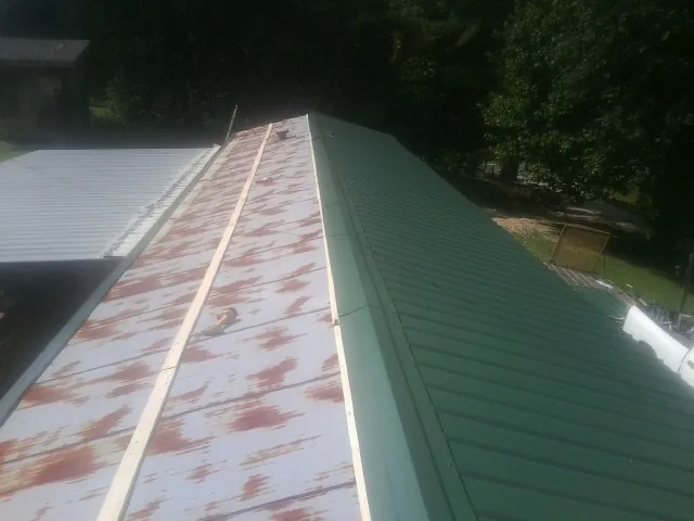 Old rusted panels beside newly installed green metal roofing — Wind Damage Roof Repair by Roofing Brothers in East Prospect