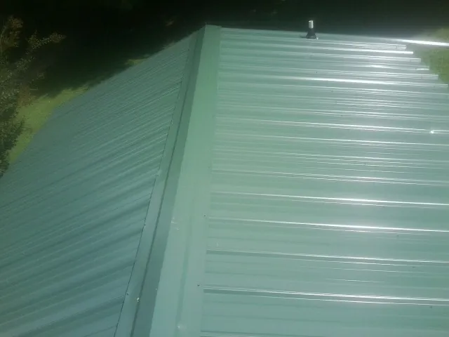New green metal panels meeting at the ridge of a roof — Flat Roof Repair work by our crew in East Prospect