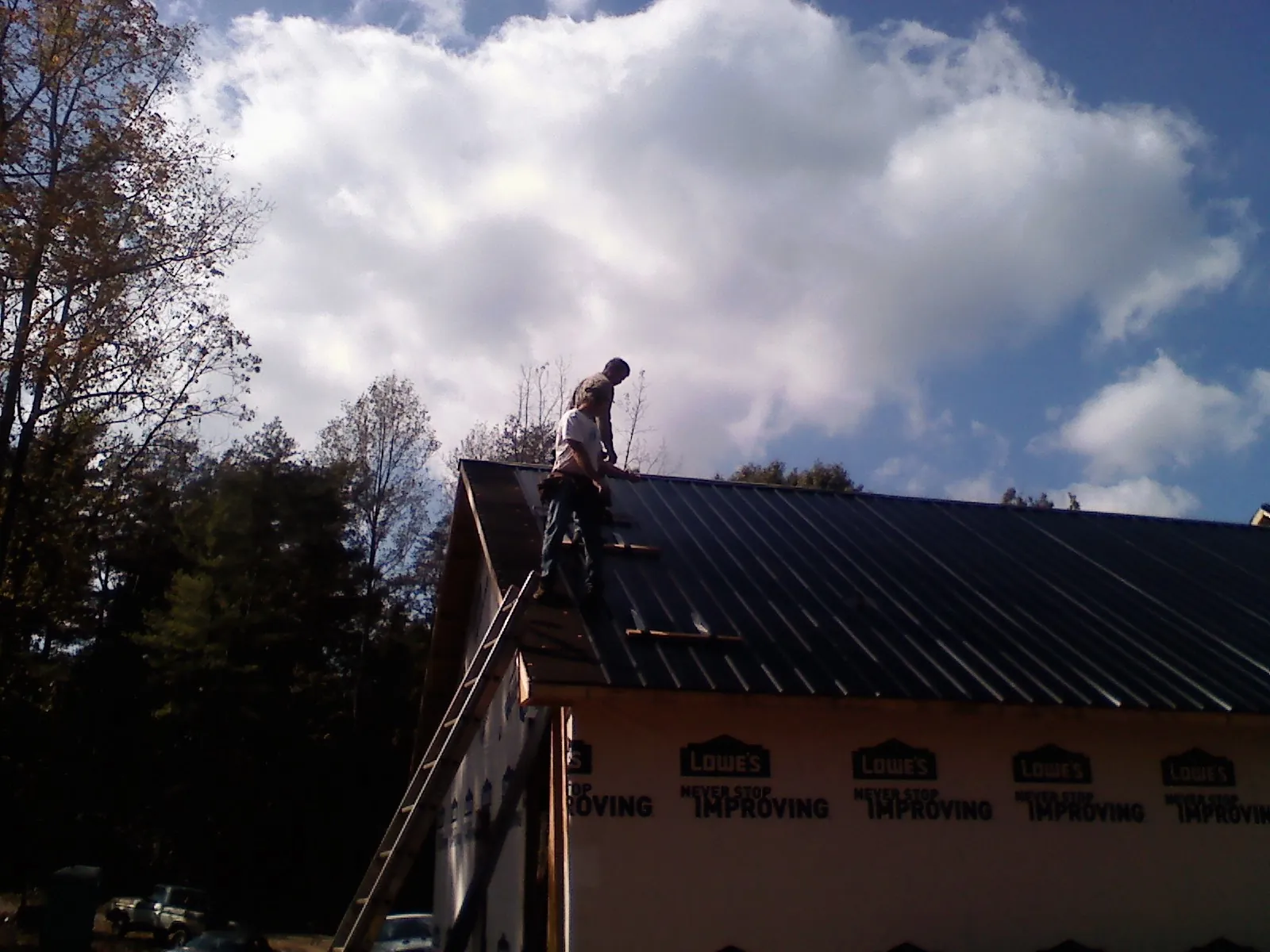 Roofer fastening dark metal panels high against a cloudy sky, from a Roof Inspection job in East Prospect
