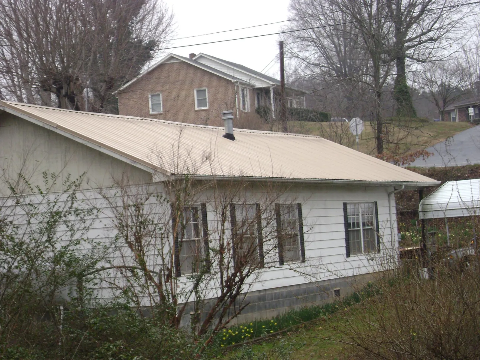 Tan metal roof on a white sided house set into a hillside — Commercial Roofing by Roofing Brothers in East Prospect
